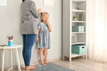 Mother measuring height of little girl near wall