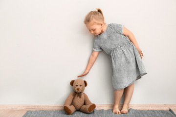 Little girl measuring height of toy bear near wall