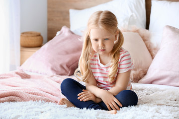 Obraz na płótnie Canvas Sad little girl sitting on bed