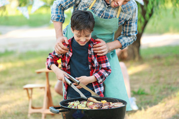 Little boy with father cooking tasty food on barbecue grill outdoors