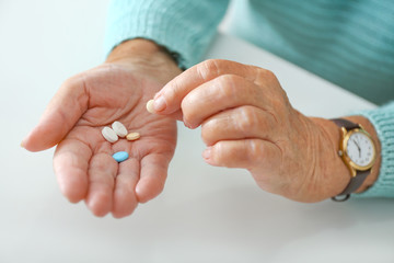 Elderly woman with pills at white table, closeup