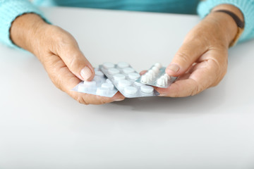 Elderly woman with pills at white table, closeup