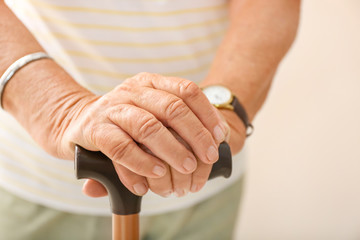 Elderly woman with walking stick on light background, closeup