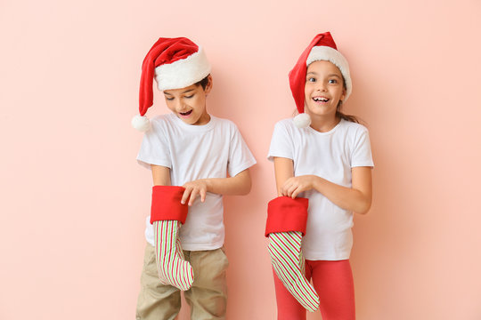 Happy little children in Santa hats and with Christmas stockings on color background