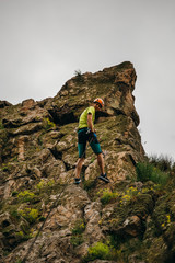 Low angle view of a man descending from the cliff against grey sky