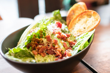 Caesar salad in black bowl on wooden table.