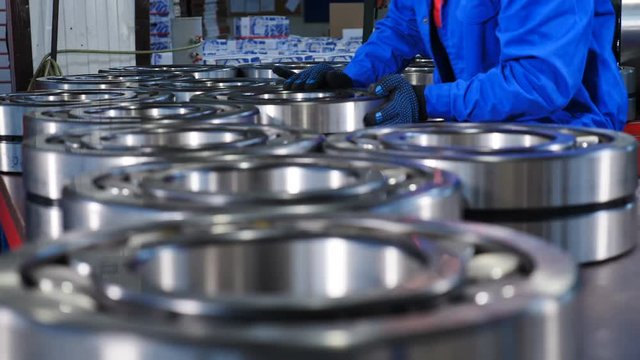 Machinery and industry concept. Set of various gears and ball large bearings, spare parts warehouse. Male worker hands in blue uniform in bearing factory. Mechanic assembles bearings. A qualified