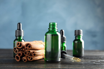 Bottles with essential oil and cinnamon sticks on wooden table against blue background