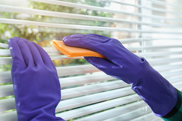 Woman cleaning window blinds with rag indoors, closeup