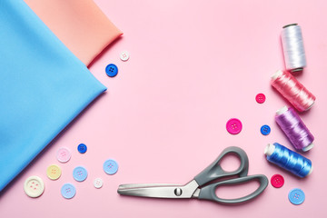 Frame made of sewing scissors, threads, buttons and fabric on pink background, flat lay. Space for...