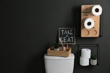 Decor elements, necessities and toilet bowl near black wall, space for text. Bathroom interior