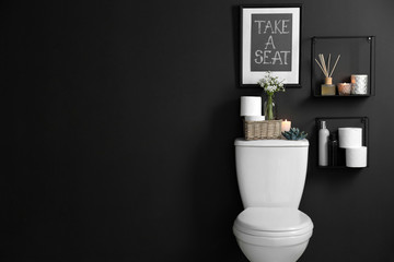 Decor elements, necessities and toilet bowl near black wall, space for text. Bathroom interior