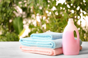 Pile of fresh towels and detergent on table against blurred background, space for text