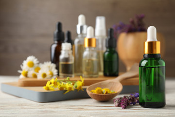 Bottles of different essential oils and wildflowers on wooden table, space for text