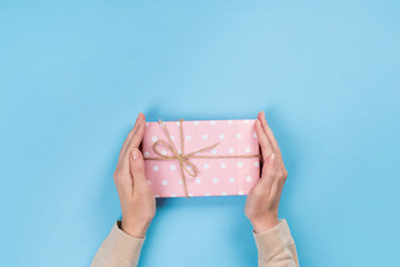 Fototapeta na wymiar Womans hands holding gift or present box on blue pastel table. Flat lay for birthday or New Year.