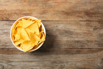 Tasty mexican nachos chips in bowl on wooden table, top view. Space for text