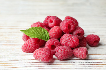 Delicious fresh ripe raspberries with leaves on white wooden table, closeup view