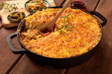 Homemade Shepherd's pie in a cooking pan with pickles and red wine on a dark rustic wooden background