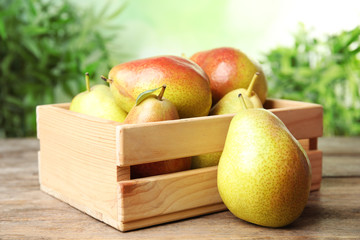 Crate with ripe juicy pears on brown wooden table against blurred background