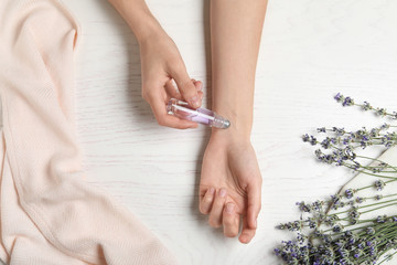 Top view of woman applying lavender essential oil at white wooden table, closeup
