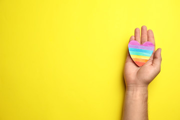 Man with rainbow heart on yellow background, top view and space for text. Gay symbol