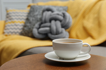 Cup of hot drink on table near sofa with pillows in living room