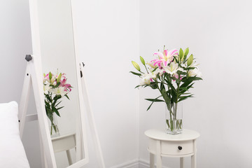 Vase with bouquet of beautiful lilies on white table near mirror
