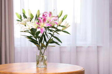 Vase with bouquet of beautiful lilies on wooden table indoors. Space for text