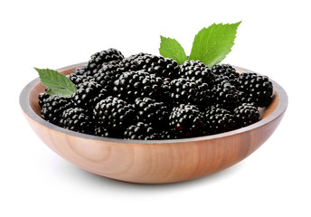 Wooden bowl of tasty ripe blackberries with leaves on white background