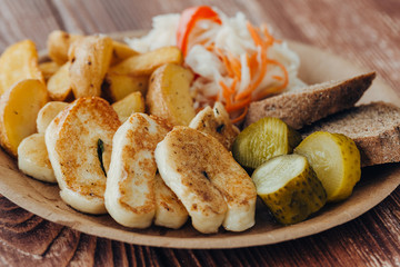 Tasty grilled fish with fried potatoes, cucumber, cabbage and woods in a paper plate on a wooden table. takeaway street food
