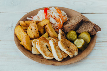 Tasty grilled fish with fried potatoes, cucumber, cabbage and woods in a paper plate on a wooden table. takeaway street food