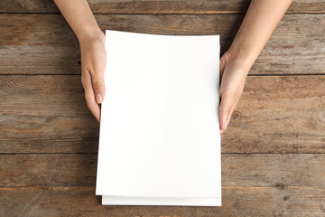 Woman holding blank paper sheets for brochure at wooden table, top view. Mock up