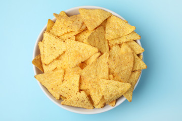Bowl of tasty Mexican nachos chips on light blue background, top view