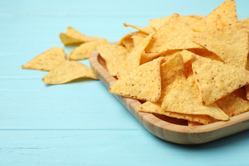 Wooden plate of tasty Mexican nachos chips on light blue wooden background
