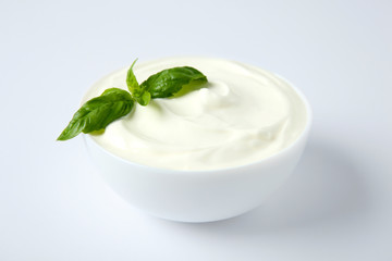 Bowl of fresh sour cream with basil on white background