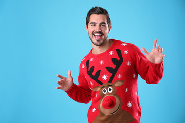 Portrait of happy young man in Christmas sweater on light blue background