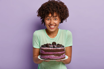 Portrait of happy dark skinned housewife demonstrates delicious cake baked by herself, wants to...