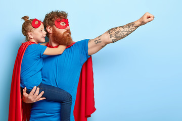Horizontal shot of young serious ginger dad possesses bravery and courgae, makes flying gesture,...