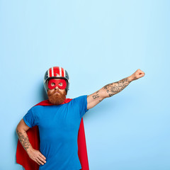 Serious confident superman pretends to fly, wears superhero costume, protective helmet, has...
