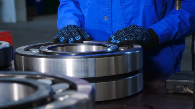 Machinery and industry concept. Set of various gears and ball large bearings, spare parts warehouse. Male worker hands in blue uniform in bearing factory. A qualified employee at plant putiing large