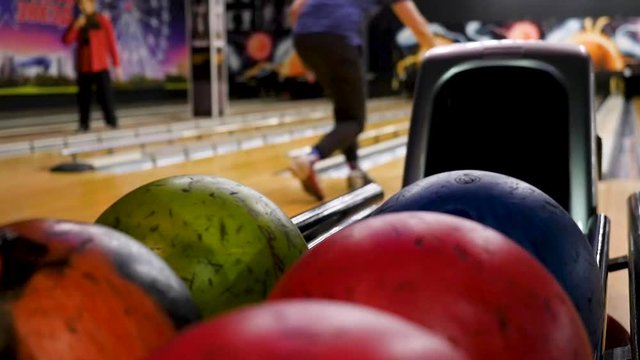 Close-up of young man taking bowling balls from the rack. Media. Competitive cheerful friends playing bowling together in the club