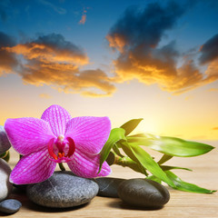 Zen pebbles with bamboo leaves and orchid flower on table, in the background sunset sky.. Spa and healthcare concept.