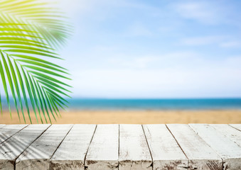 White wood table top with blur sea beach and coconut leaf.Holiday summer background