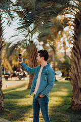 Image of handsome young man wearing coat talking on smartphone and smiling at camera while walking