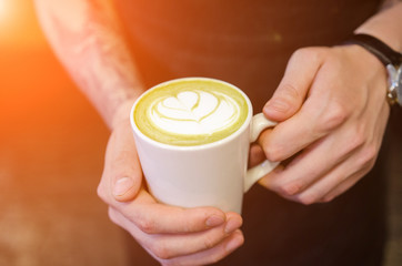 Closeup image of male hands holding cup of matcha latte