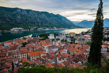 Naklejka na ściany i meble Montenegro, Aerial view over the roofs of old town of kotor bay and coastal waterside of fjord surrounded by mountains in magical evening sunset twilight