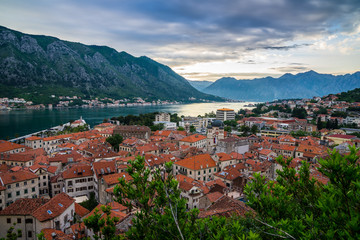 Montenegro, View above roofs of beautiful old town of kotor bay next to waterside of fjord surrounded by mountains in magical sunset twilight atmosphere