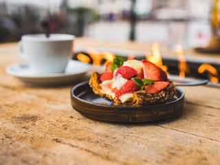 Delicious  crispy pastry with fresh strawberries and a cup of coffee on the table with fire. Outdoor terrace of cafe in Zierikzee, Netherlands.