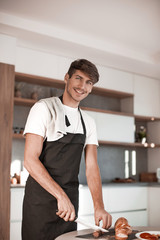 attractive young man slicing sausage for sandwiches