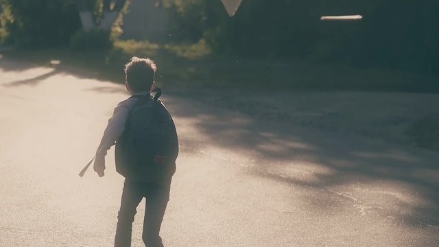 young guy with schoolbag jumps on grey asphalt road and throws up sheets when skips school slow motion backside view